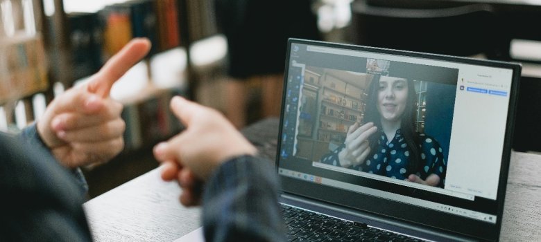 Im Fokus ein Laptop; auf dem Bildschirm eine Person, die in Gebärdensprache spricht