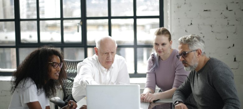 Zwei jüngere Personen unterstützen zwei ältere Personen in der Bedienung eines Laptops